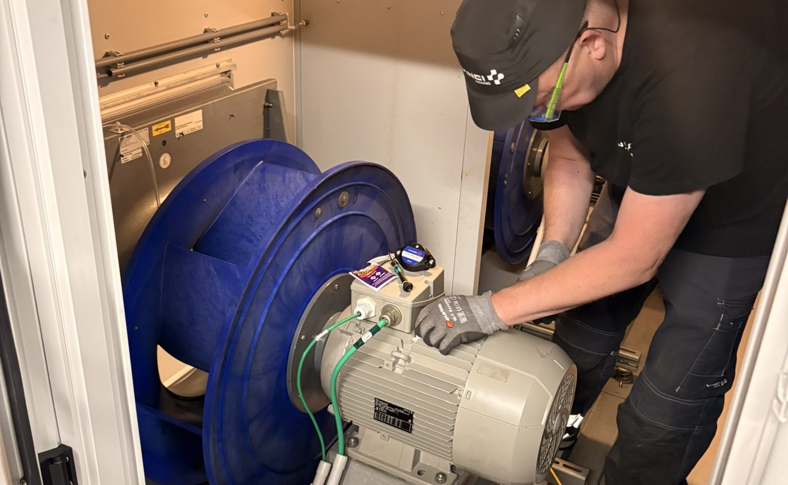 An XCVBN technician installing a predictive maintenance sensor on an industrial fan motor.